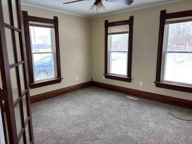 carpeted empty room with ornamental molding, visible vents, ceiling fan, and baseboards