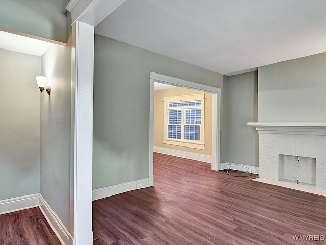 unfurnished living room with a brick fireplace, baseboards, and dark wood-style flooring