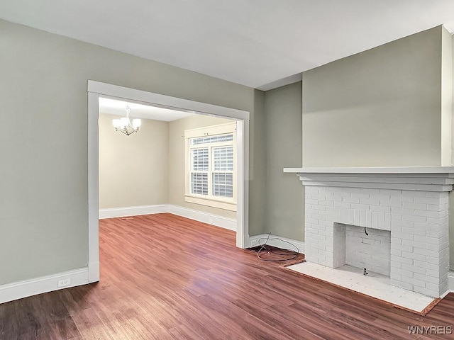 unfurnished living room with a brick fireplace, baseboards, a chandelier, and wood finished floors