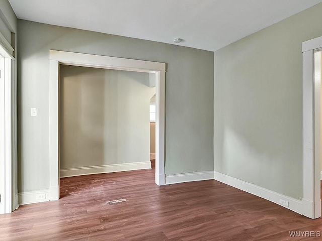 spare room with dark wood-type flooring, visible vents, and baseboards