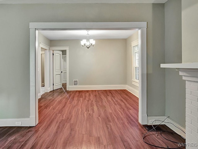 unfurnished dining area featuring a notable chandelier, baseboards, and wood finished floors