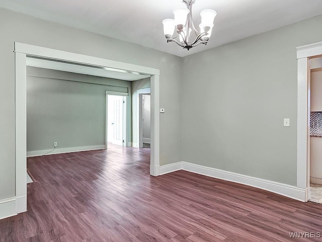 unfurnished room with a notable chandelier, baseboards, and wood finished floors