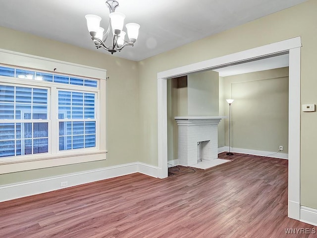 unfurnished living room featuring a brick fireplace, wood finished floors, and baseboards