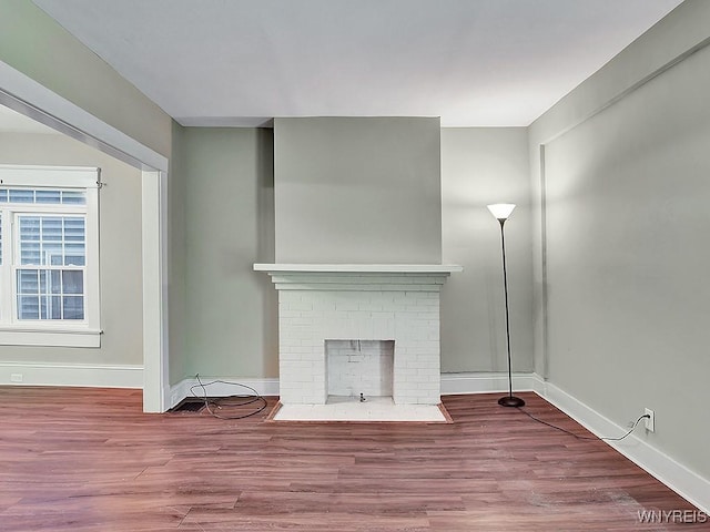 unfurnished living room featuring a fireplace, baseboards, and wood finished floors