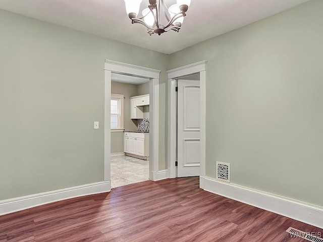 empty room with baseboards, light wood-style flooring, visible vents, and a notable chandelier