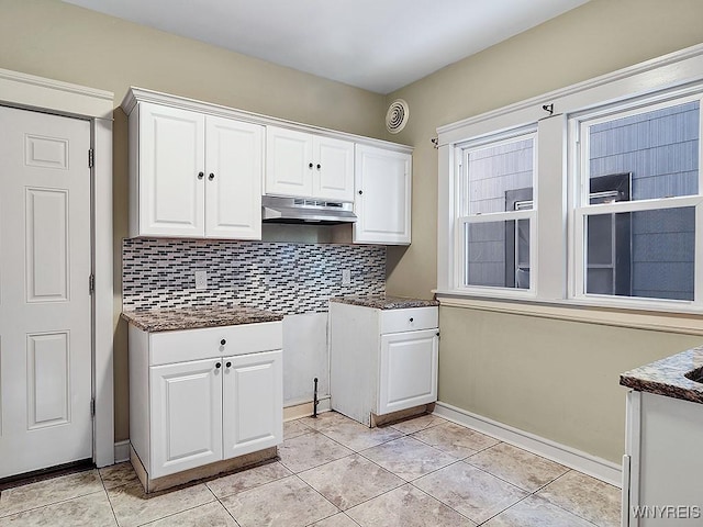 kitchen with light tile patterned floors, dark countertops, backsplash, white cabinetry, and under cabinet range hood