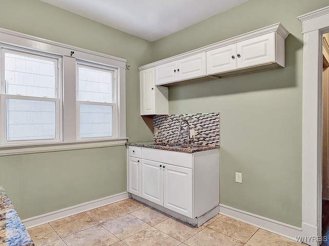 kitchen with a sink, baseboards, white cabinets, backsplash, and dark stone countertops