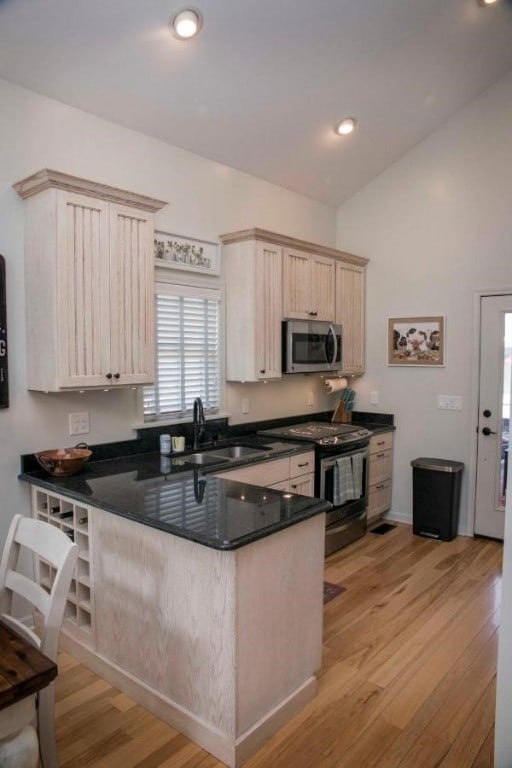 kitchen with light brown cabinets, a peninsula, a sink, appliances with stainless steel finishes, and light wood-type flooring