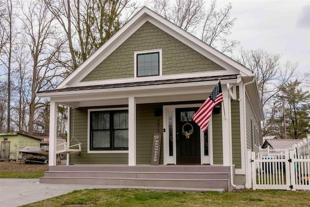 bungalow featuring covered porch, fence, and a standing seam roof