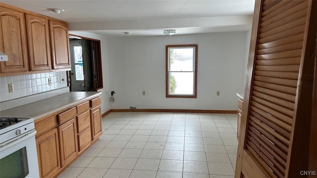 kitchen with baseboards, light countertops, decorative backsplash, and white gas range oven