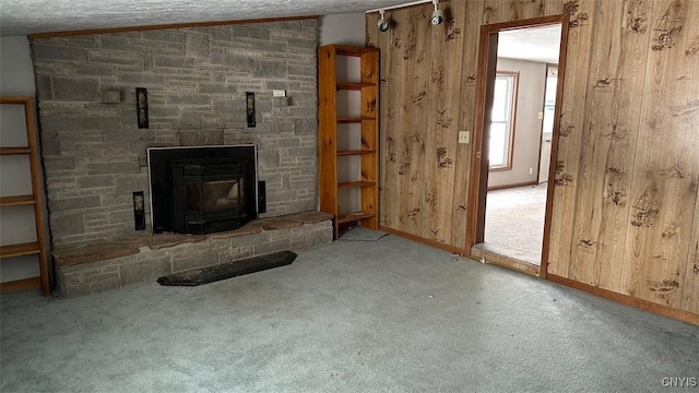 unfurnished living room with wooden walls, baseboards, light colored carpet, a wood stove, and vaulted ceiling