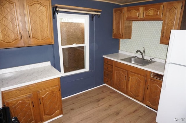 kitchen with brown cabinetry, freestanding refrigerator, light countertops, light wood-type flooring, and a sink