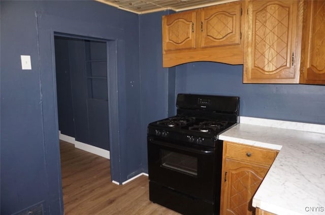 kitchen with black range with gas cooktop, baseboards, brown cabinets, wood finished floors, and light countertops