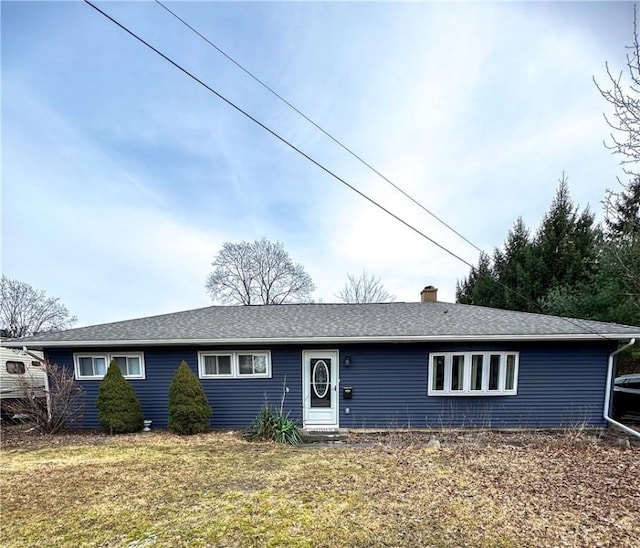 ranch-style home featuring entry steps, a shingled roof, a chimney, and a front yard