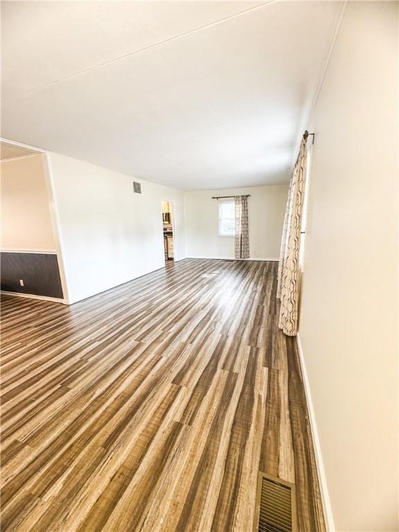 unfurnished living room featuring visible vents, baseboards, and wood finished floors