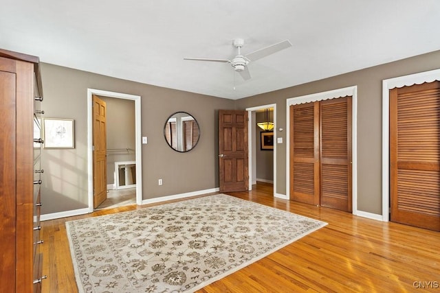 unfurnished bedroom featuring baseboards, light wood finished floors, ensuite bathroom, and multiple closets