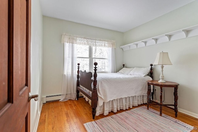 bedroom featuring a baseboard heating unit, light wood-type flooring, and baseboards