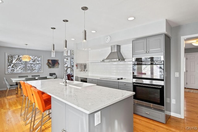 kitchen with island exhaust hood, light stone counters, gray cabinets, and a kitchen island with sink