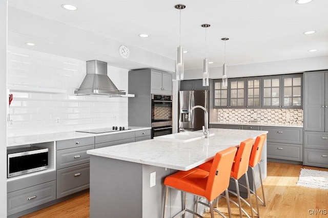 kitchen featuring glass insert cabinets, appliances with stainless steel finishes, a kitchen island with sink, light stone countertops, and extractor fan