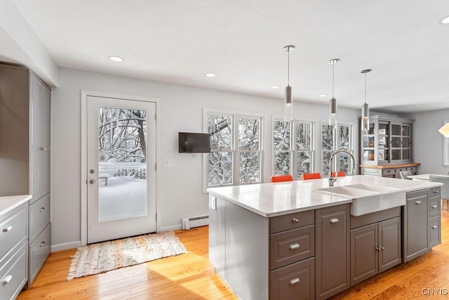 kitchen featuring a sink, light wood-style floors, hanging light fixtures, baseboard heating, and a center island with sink