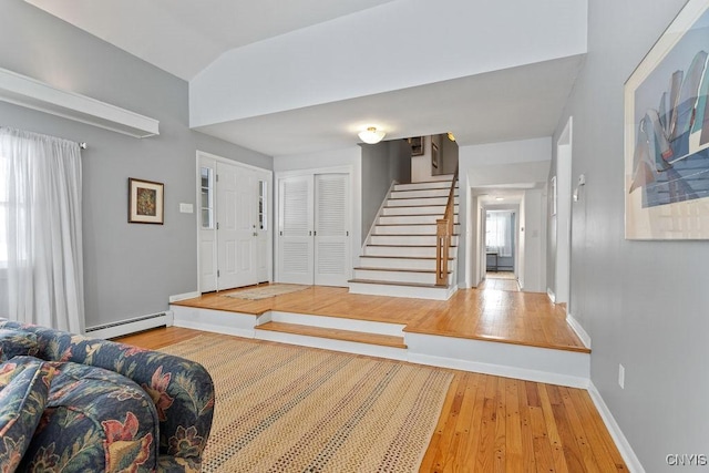 entrance foyer with light wood finished floors, baseboards, lofted ceiling, a baseboard radiator, and stairs