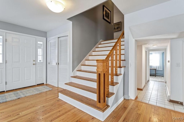 foyer featuring light wood finished floors, stairway, a baseboard radiator, and baseboards