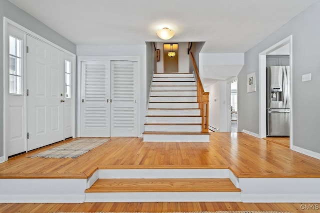 foyer entrance with stairs, baseboards, baseboard heating, and a wealth of natural light