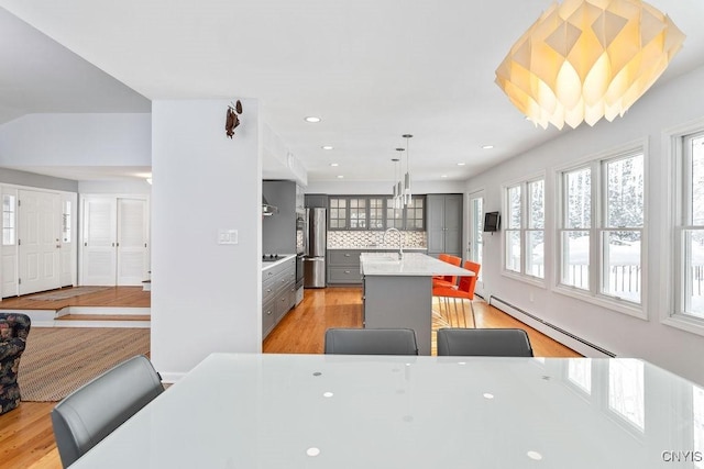 kitchen with glass insert cabinets, decorative light fixtures, light countertops, a kitchen bar, and a baseboard heating unit