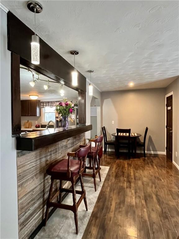 bar with a textured ceiling, baseboards, hanging light fixtures, hardwood / wood-style floors, and rail lighting