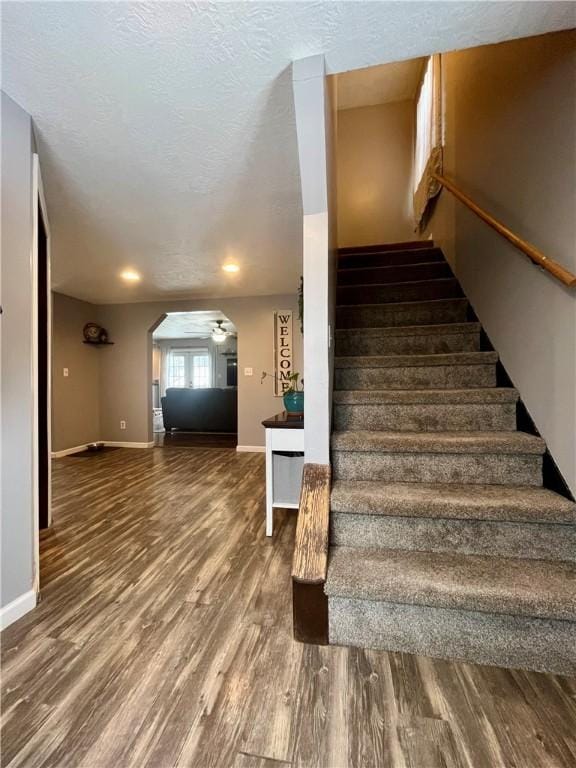 stairs featuring arched walkways, ceiling fan, a textured ceiling, wood finished floors, and baseboards