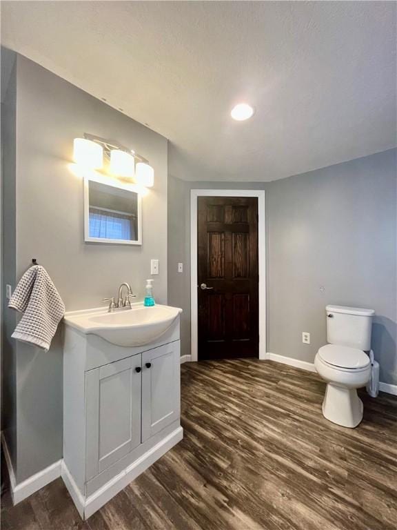 bathroom featuring toilet, vanity, baseboards, and wood finished floors