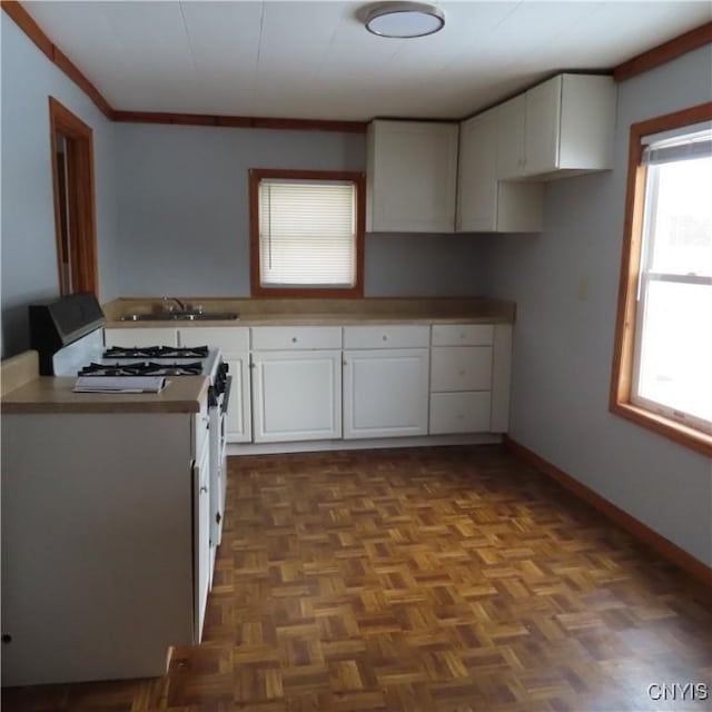 kitchen featuring stainless steel gas range oven, a sink, white cabinetry, baseboards, and ornamental molding