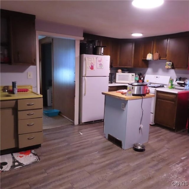 kitchen featuring white appliances, a center island, light countertops, dark brown cabinets, and light wood-style floors