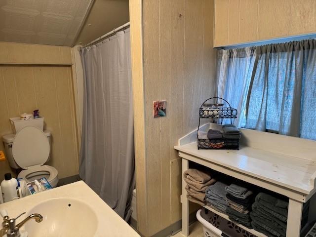 bathroom featuring wooden walls, toilet, a shower with shower curtain, and a sink