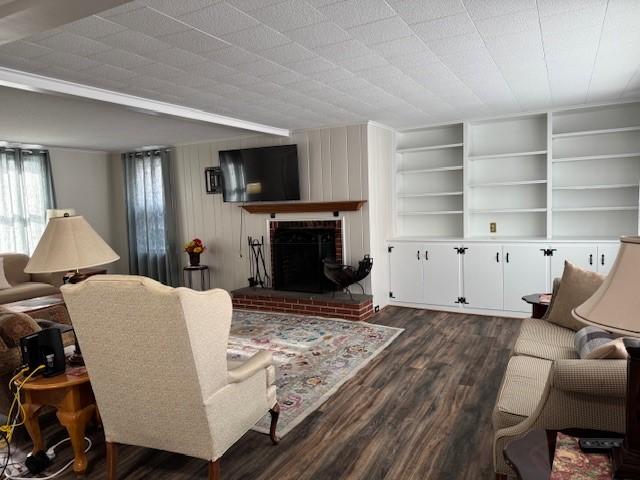 living room featuring a brick fireplace, built in features, dark wood-style flooring, and wood walls