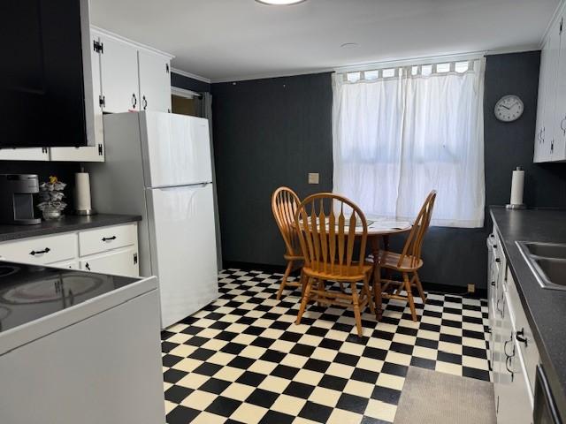 kitchen with light floors, freestanding refrigerator, white cabinetry, dark countertops, and range