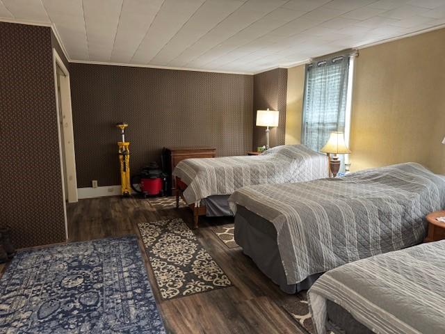 bedroom featuring wood finished floors, crown molding, and wallpapered walls