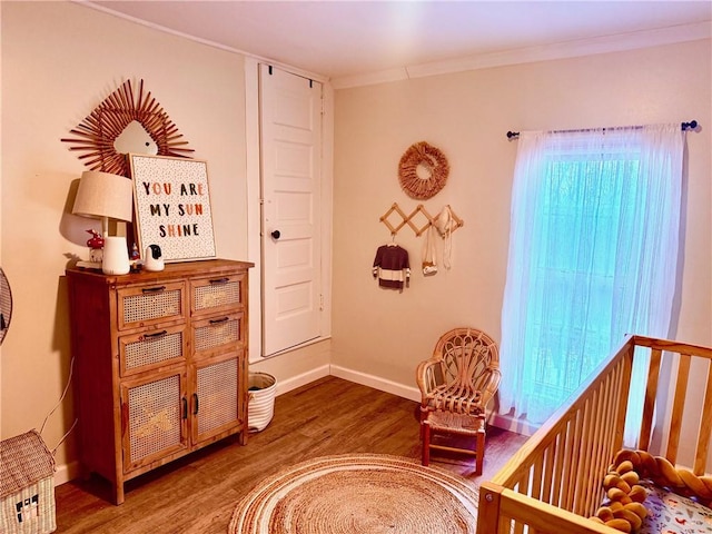 bedroom with a nursery area, ornamental molding, wood finished floors, and baseboards