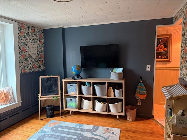 recreation room with wainscoting, baseboard heating, and wood finished floors