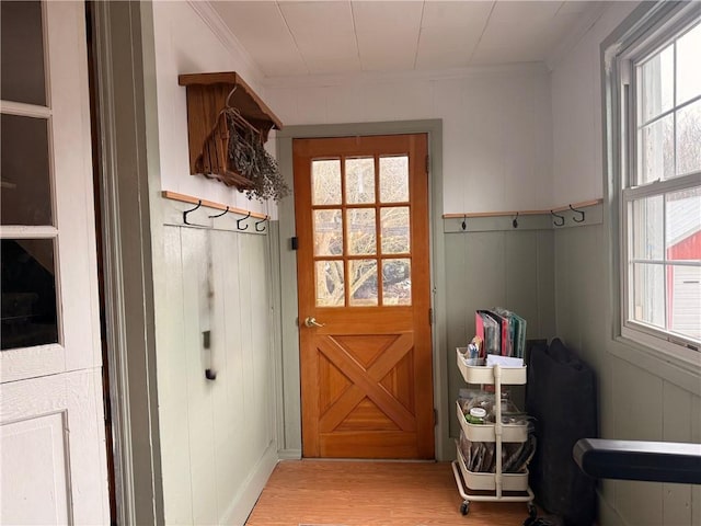 entryway featuring light wood-style floors, a decorative wall, and crown molding