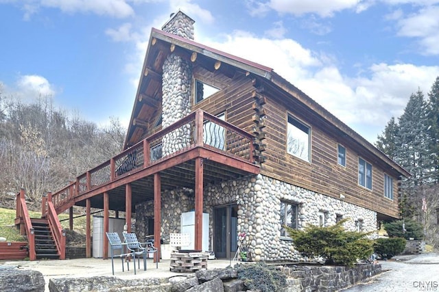 exterior space featuring a chimney, stairway, a patio area, log exterior, and a wooden deck