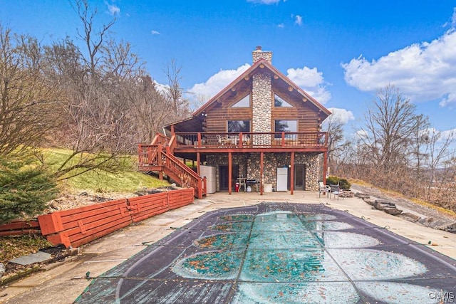 rear view of property with a chimney, a patio area, log exterior, a wooden deck, and stairs