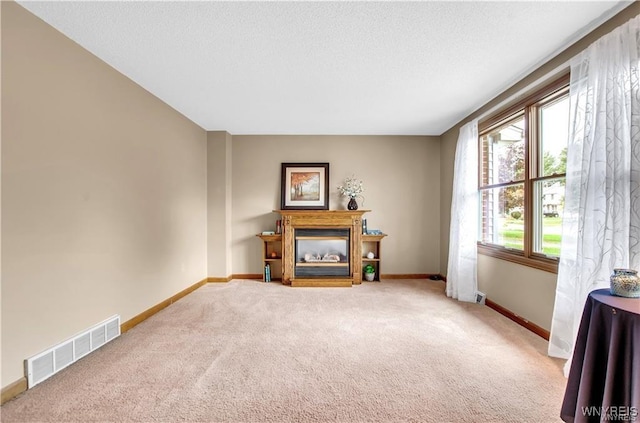 living room with carpet flooring, a glass covered fireplace, visible vents, and baseboards