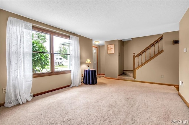 carpeted empty room with a textured ceiling, baseboards, and stairs