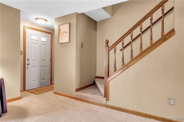 foyer entrance featuring light colored carpet, baseboards, and stairs