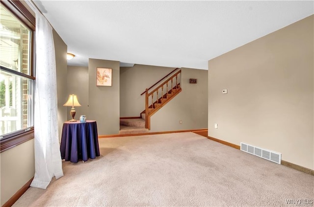 carpeted empty room featuring stairs, visible vents, and baseboards