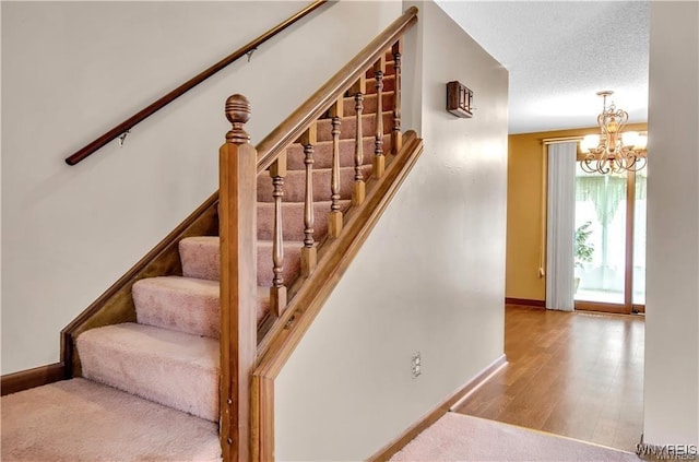 stairway featuring an inviting chandelier, baseboards, a textured ceiling, and wood finished floors