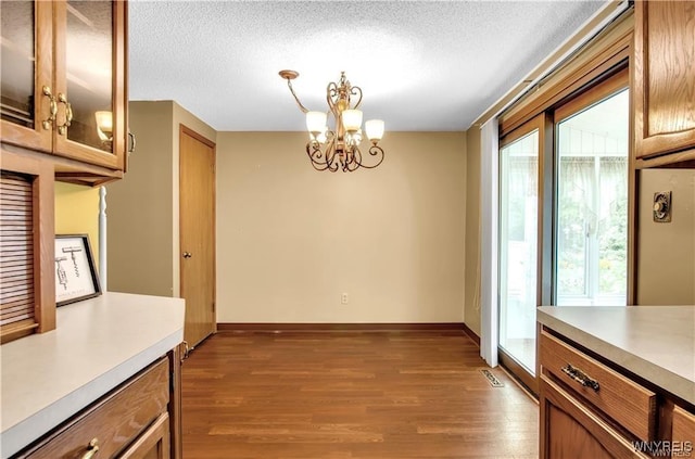 unfurnished dining area with a notable chandelier, a textured ceiling, baseboards, and wood finished floors