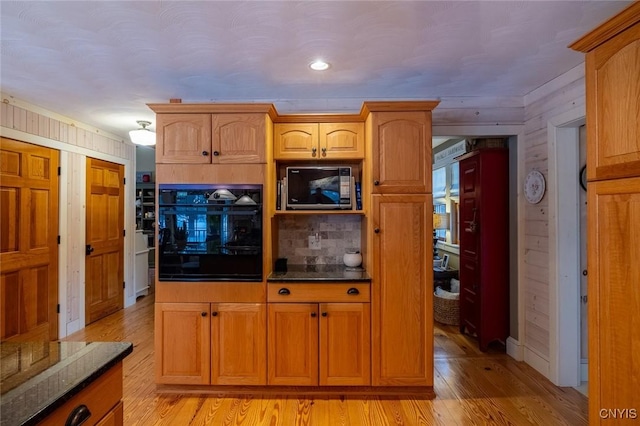 kitchen with light wood-style flooring, brown cabinets, dark stone counters, black appliances, and tasteful backsplash