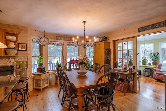 dining area with wood walls, light wood-style flooring, and an inviting chandelier